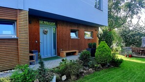 Ein modernes, zweistöckiges Haus mit Holzfassade, einer blauen Tür und einer kleinen Veranda mit einer Bank.