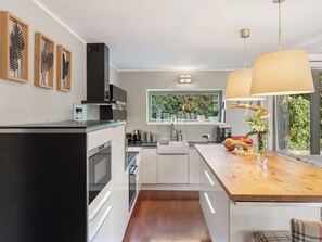 A modern kitchen with white cabinetry, a wooden countertop, and a large window with a view of greenery.