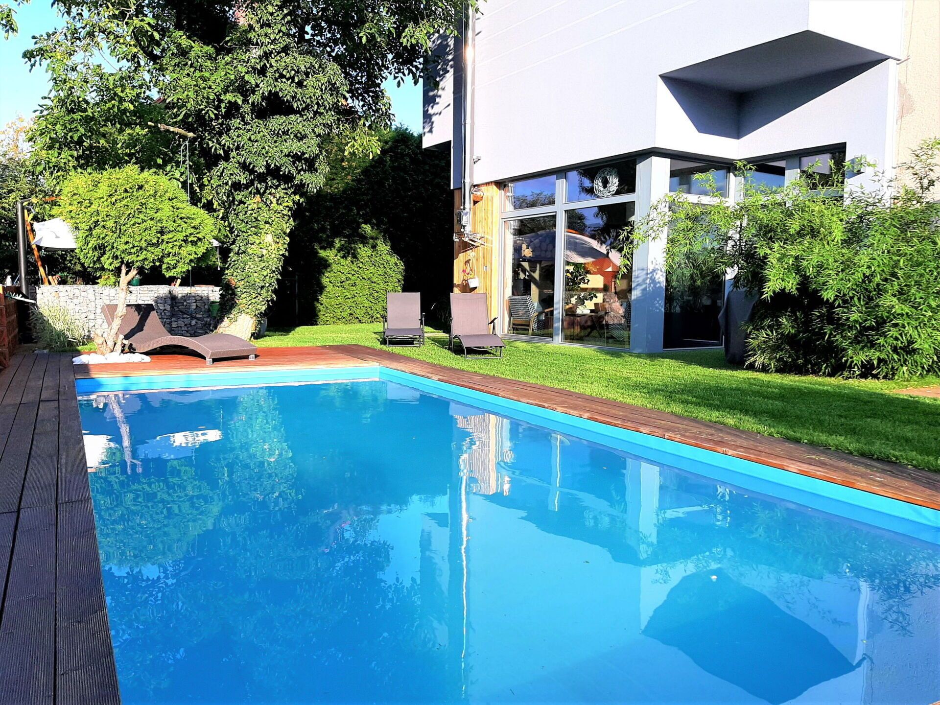 Une piscine moderne à l’eau d’un bleu limpide, entourée d’une terrasse en bois et d’une pelouse bien entretenue.