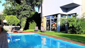 Ein moderner Pool mit klarem, blauem Wasser, umgeben von einer Holzterrasse und einem gepflegten Rasen.