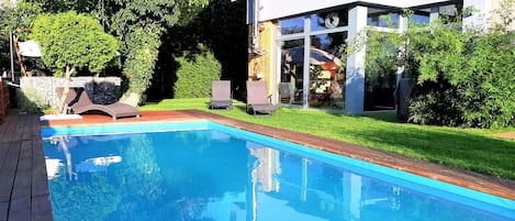 A modern pool with clear blue water, surrounded by a wooden deck and a well-maintained lawn.