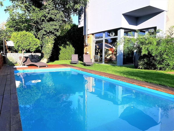 A modern pool with clear blue water, surrounded by a wooden deck and a well-maintained lawn.
