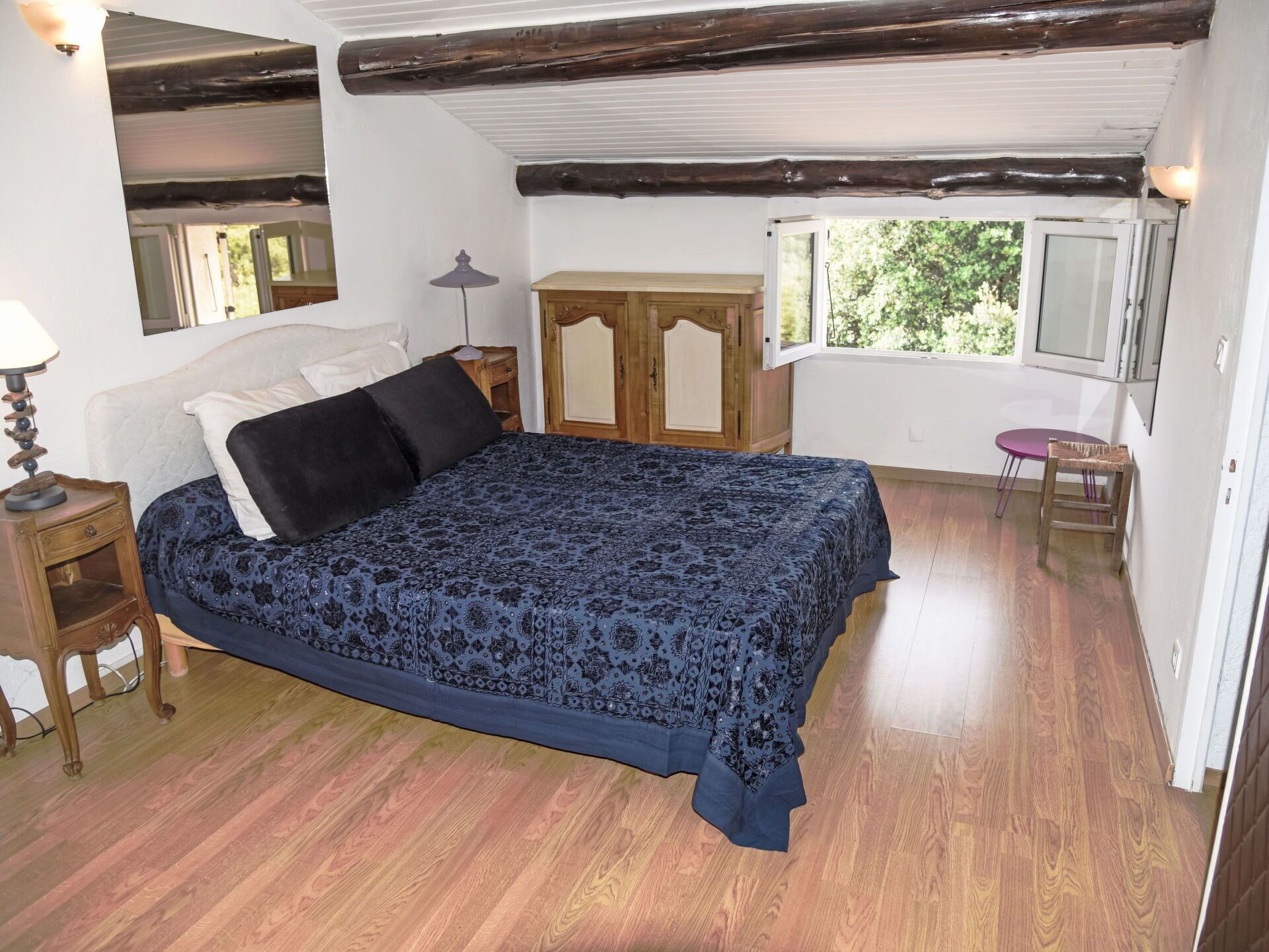 Une chambre à coucher comprenant un lit, une tête de lit en bois, une table de chevet, une commode, une fenêtre et une petite table avec une chaise.