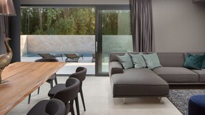 Una sala moderna con sofá, una mesa de comedor con sillas y vista a una piscina y follaje exterior.