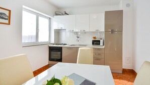 Cozinha moderna com armários brancos, fogão a gás, micro-ondas e geladeira. Há uma janela que proporciona iluminação natural e uma mesa de jantar com cadeiras.