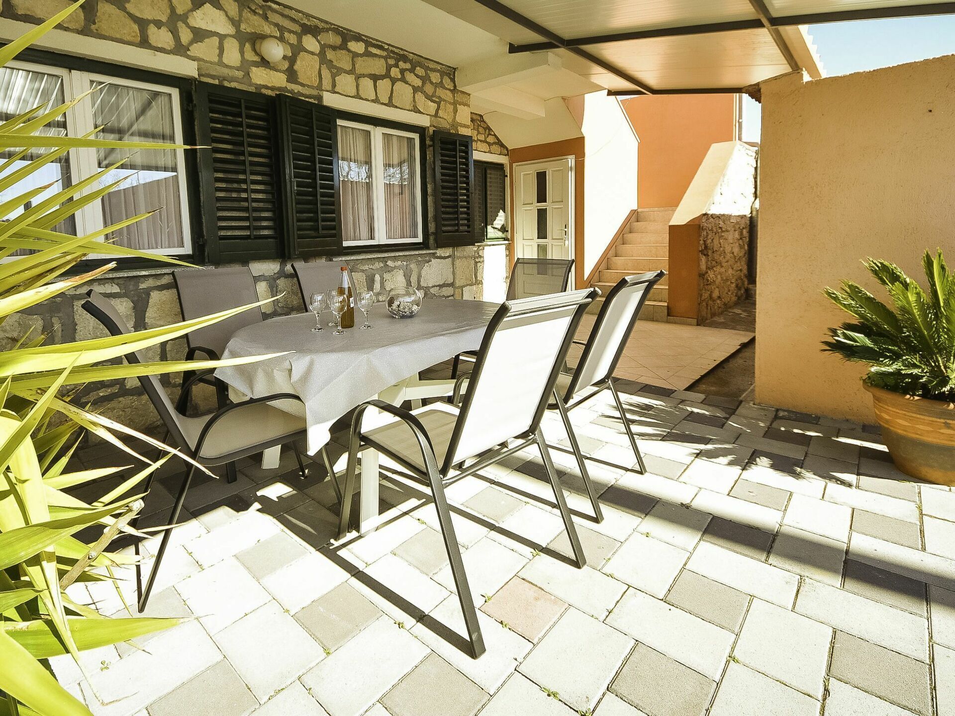 An outdoor patio with a table set for dining, stone walls, and a staircase leading to an upper level.