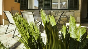 Um pátio externo com parede de pedra, uma mesa com cadeiras e plantas verdes em primeiro plano.
