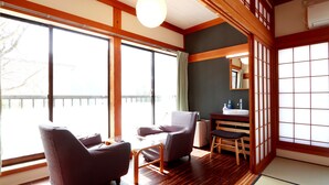 A traditional Japanese-style room with tatami flooring, a low wooden table, and two cushioned chairs. - Gokayama Ryokan Yoshinoya (Nanto)