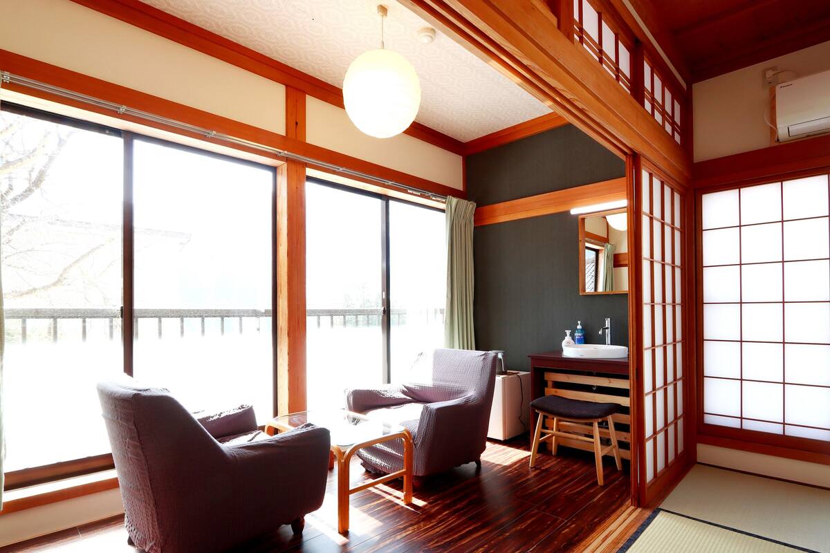 A traditional Japanese-style room with tatami flooring, a low wooden table, and two cushioned chairs.