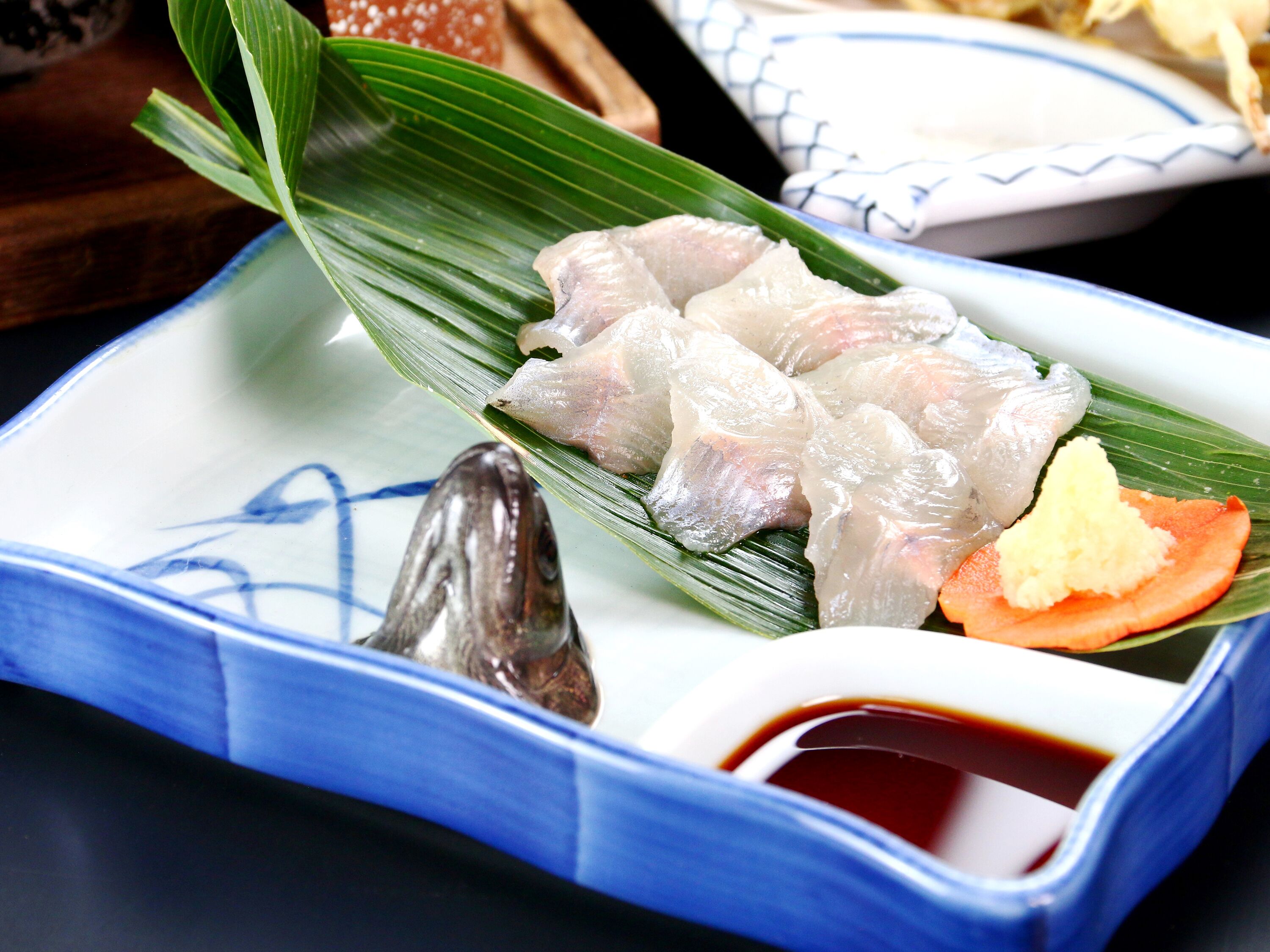 Une assiette de sashimi présentée sur une feuille, accompagnée d’un petit bol de sauce soja.