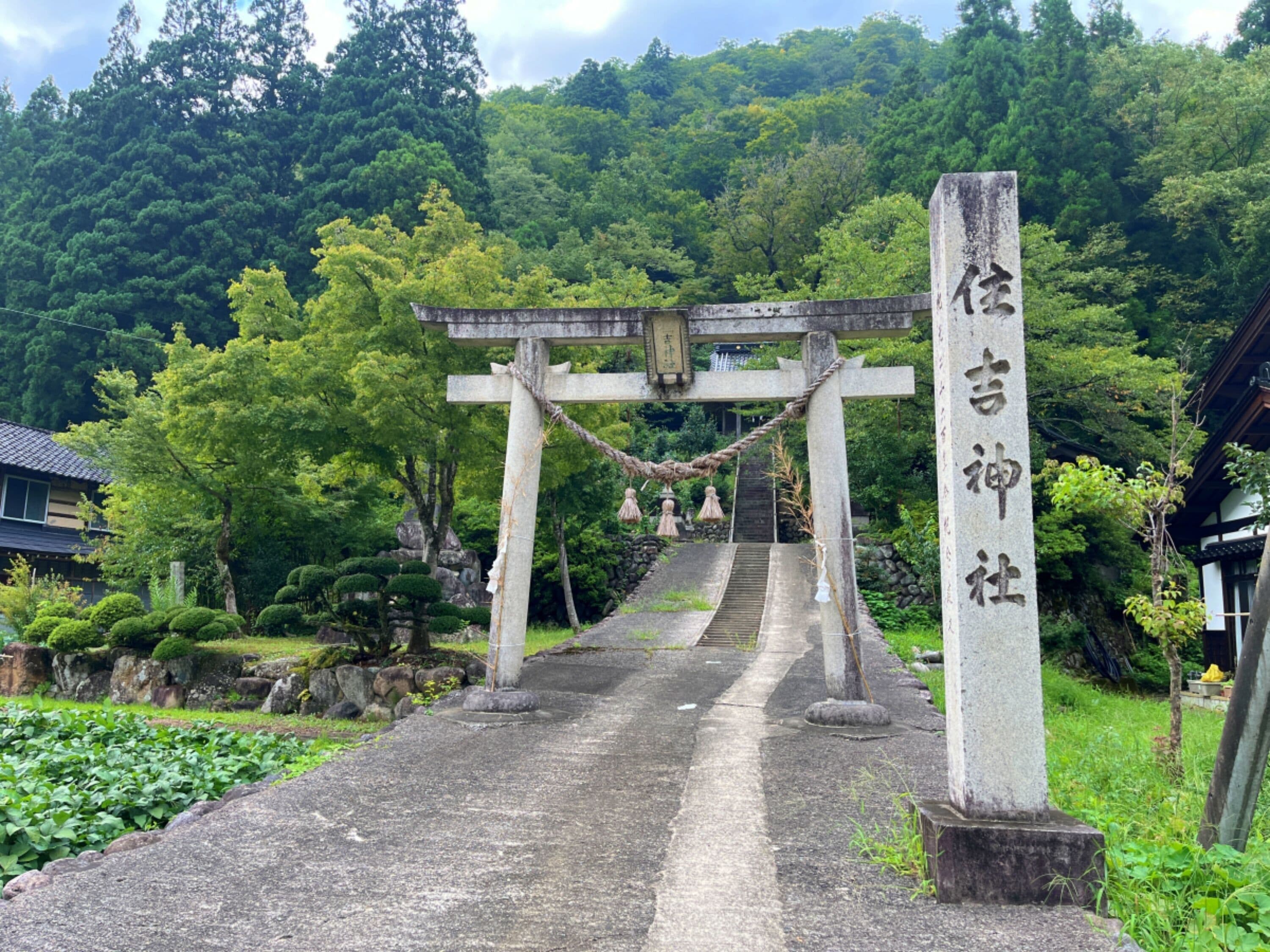 A traditional Japanese torii gate leading to a shrine, surrounded by lush greenery and a stone pathway.