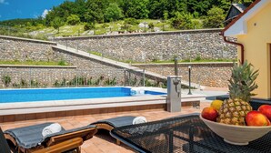 A pool area with a stone wall, lounge chairs, and a fruit bowl. - Lovely apartment for 4 people with WIFI, pool, TV, terrace and pets allowed (Senj)