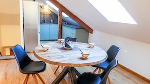 A round dining table with four black chairs, a coffee pot, and three bowls with spoons. The room has wooden flooring and a sloped ceiling with skylight. - Cosy apartment for 4 people with hot tub, WIFI and TV (Chamonix)