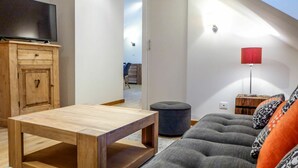 A modern living room with a wooden coffee table, grey sofa with patterned cushions, a television on a wooden cabinet, and a red floor lamp. - Cosy apartment for 4 people with hot tub, WIFI and TV (Chamonix)