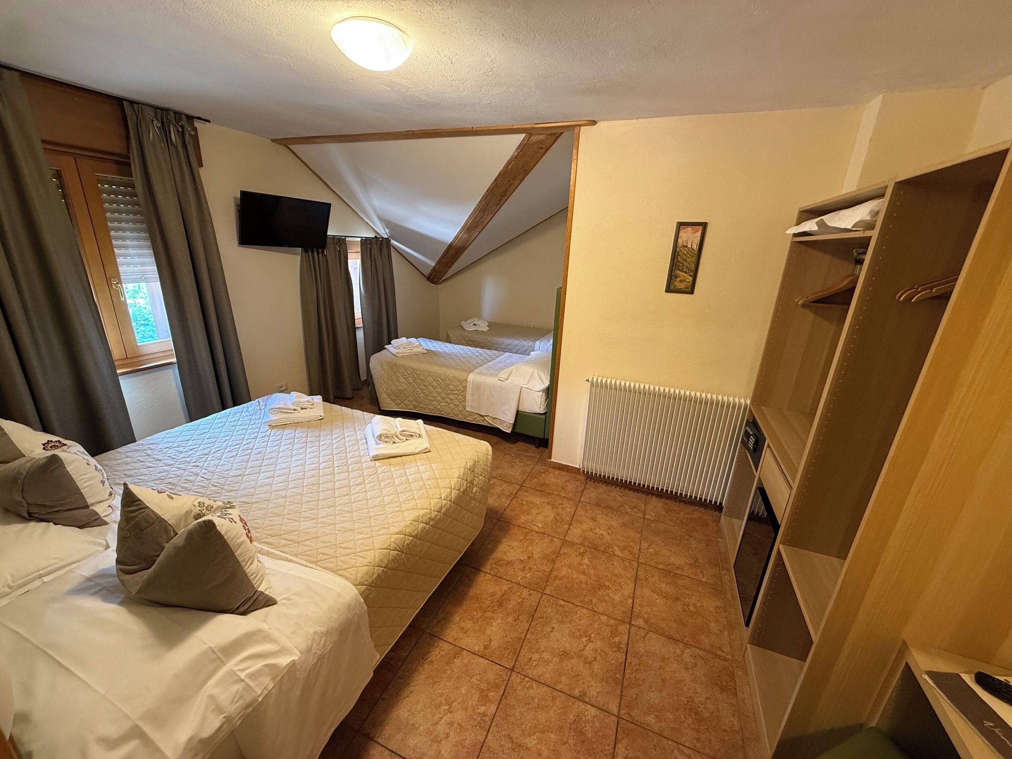 Une chambre d’hôtel avec deux lits, une télévision, un radiateur et une armoire.