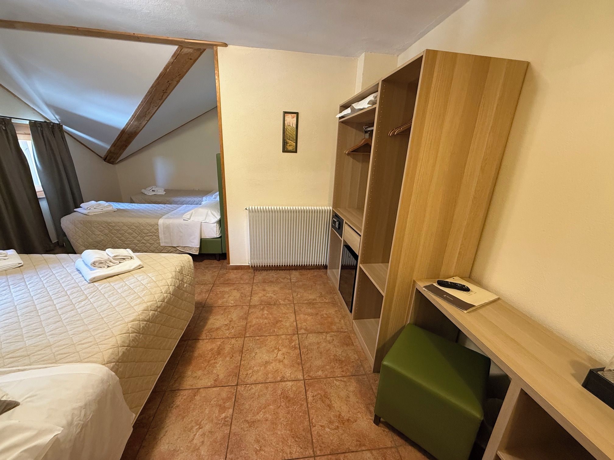 Habitación de hotel con dos camas, un radiador, un armario de madera y un banco verde.
