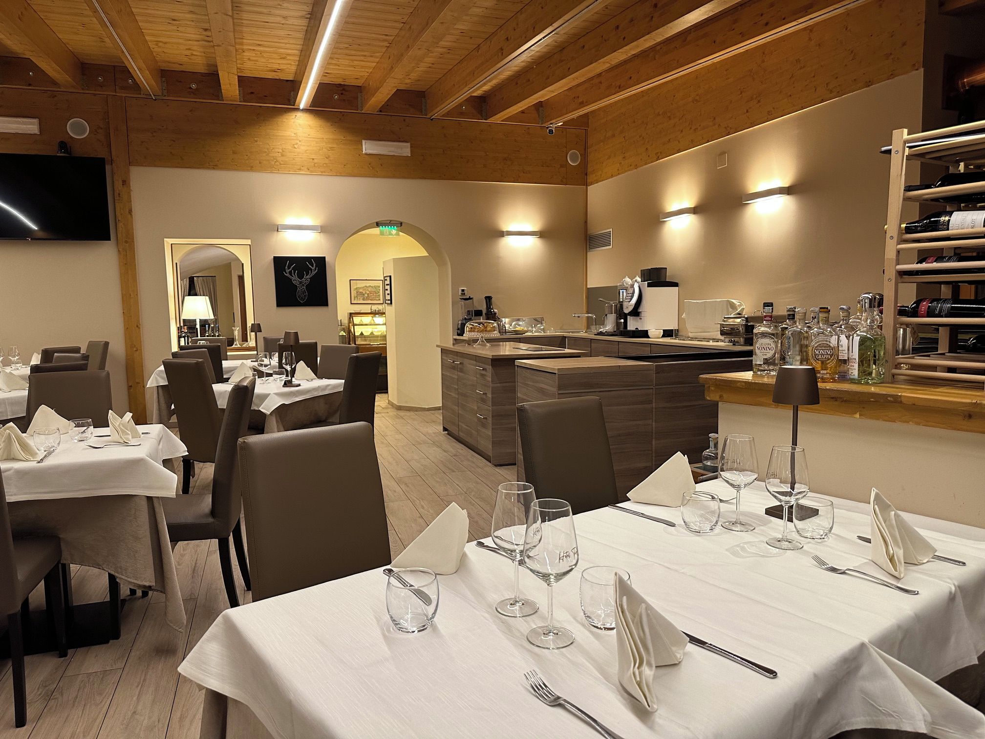Restaurante com várias mesas preparadas para refeições, área de bar com garrafas e cozinha ao fundo.