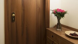 A wooden door with a brass handle and a keyhole, a vase with pink flowers on a wooden dresser, and a framed picture on the wall. - Hotel Trieste (Tarvisio)