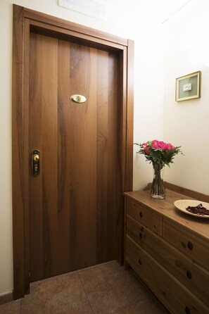 A wooden door with a brass handle and a keyhole, a vase with pink flowers on a wooden dresser, and a framed picture on the wall. - Hotel Trieste (Tarvisio)