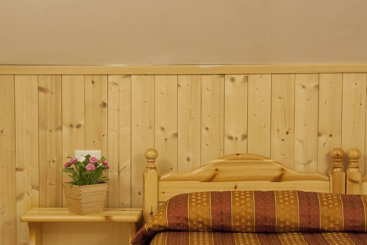 Una cama de madera con colcha a rayas, una mesita de noche de madera con un florero y un aparador de madera.