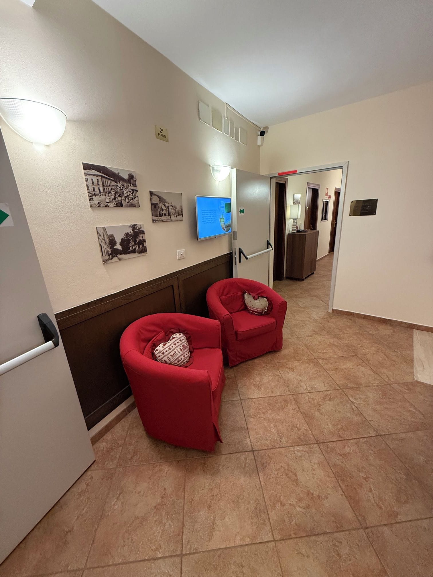 Un pasillo con dos sillones rojos, un televisor montado en la pared y una puerta que da a otra habitación.