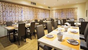 A hotel dining area with multiple tables, chairs, and a large window with curtains. - Hotel Trieste (Tarvisio)