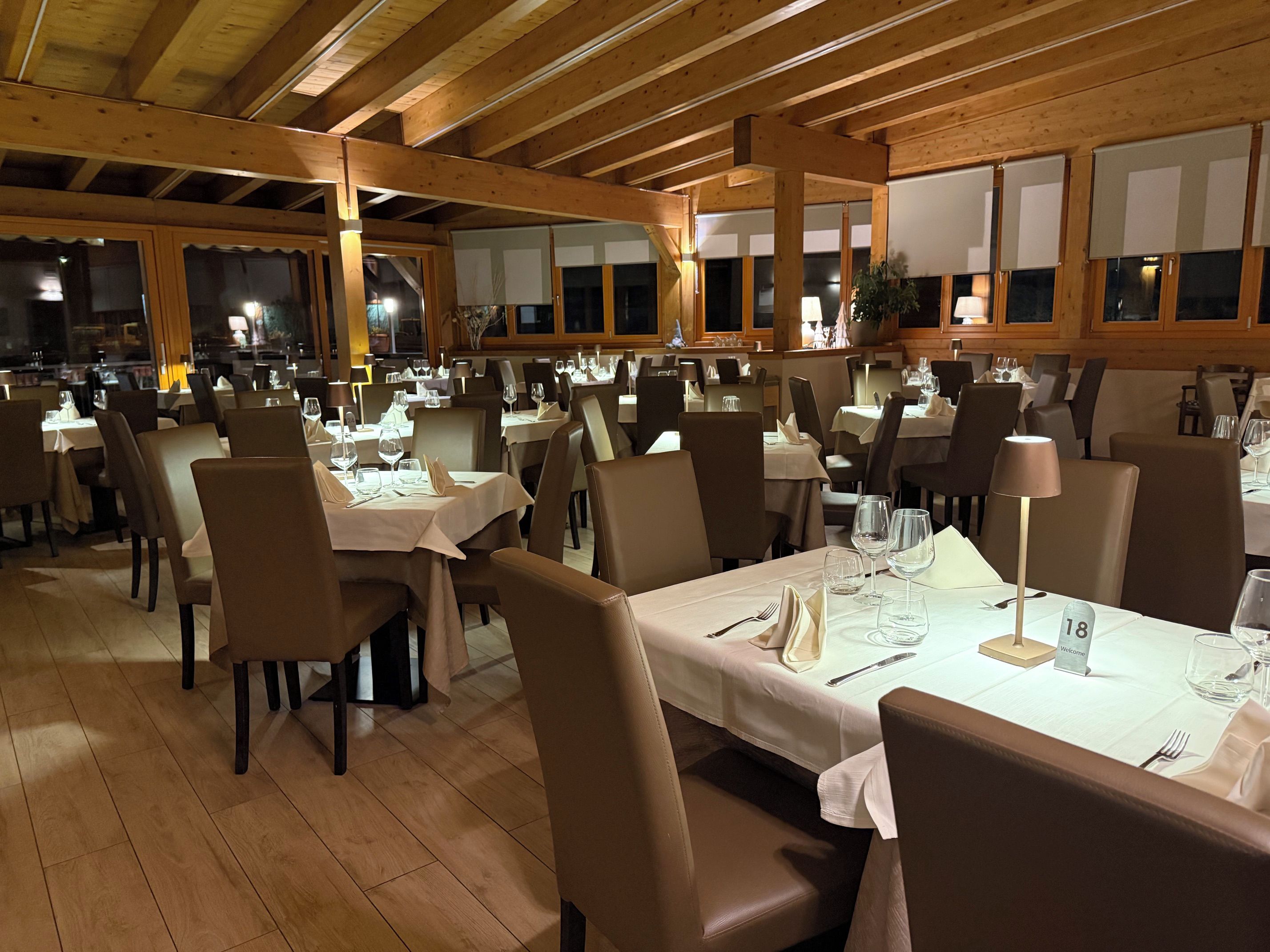 A restaurant with multiple tables and chairs, wooden beams on the ceiling, and a welcoming atmosphere.
