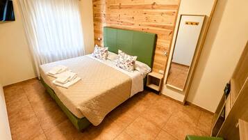 A hotel room with a bed, a green headboard, a bedside table, a mirror, and a green bench.