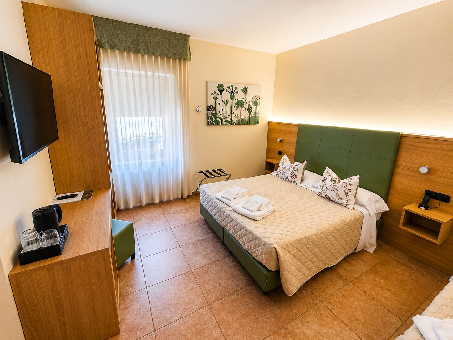A hotel room with a bed, a television, a coffee maker, and a painting on the wall.