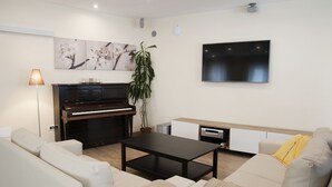 A modern living room with a piano, a flat-screen TV, a sofa, and a coffee table. - Hotel Trieste (Tarvisio)
