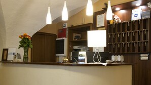 A hotel reception area with a curved counter, a vase of flowers, a desk with a computer and a lamp, and a wall-mounted key rack. - Hotel Trieste (Tarvisio)