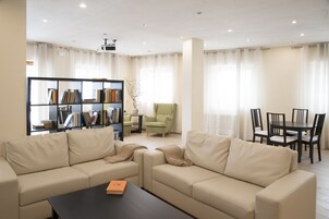 Uma sala de estar moderna com um sofá bege, uma mesa de centro, uma estante, uma poltrona verde e uma área de jantar com mesa e cadeiras.
