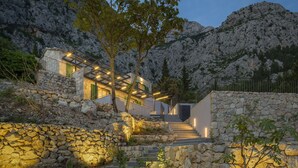 A modern house with stone walls and a staircase leading to a wooden deck.