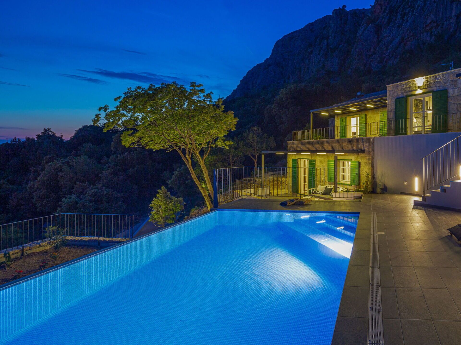 A modern poolside area with a clear blue pool, a tree, and a two-story building with balconies.