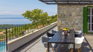A terrace with a table and chairs, a stone wall, a green door, and a view of a body of water.