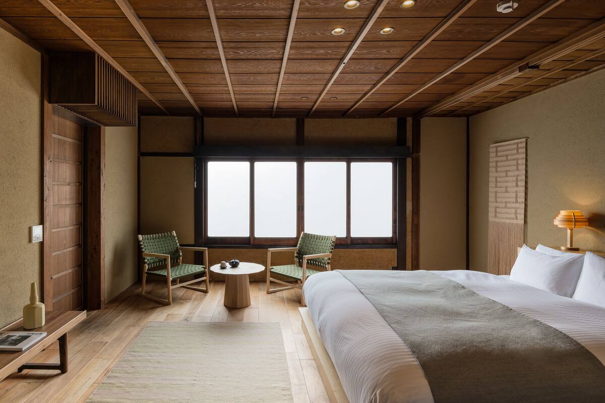 Une chambre avec un grand lit, deux chaises, une petite table et une fenêtre donnant sur un beau paysage.