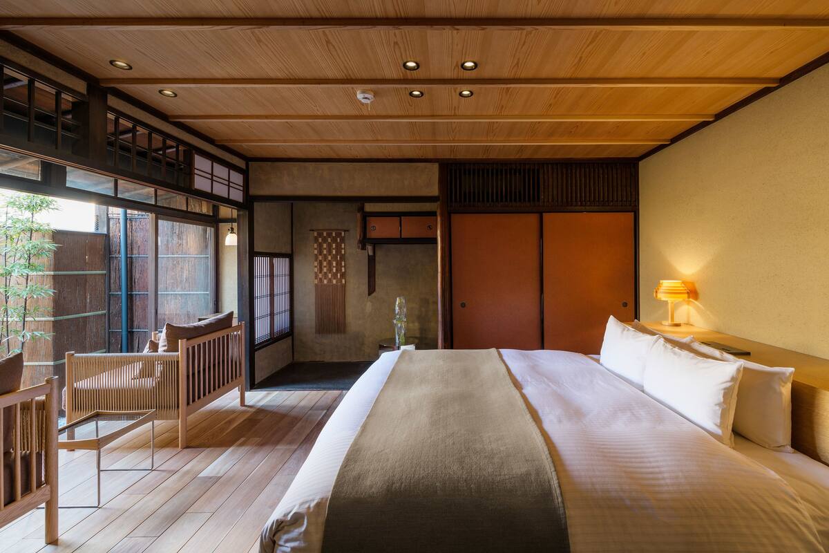 Une pièce de style japonais traditionnel, dotée d’un grand lit, d’un plancher en bois et offrant une vue sur l’extérieur.