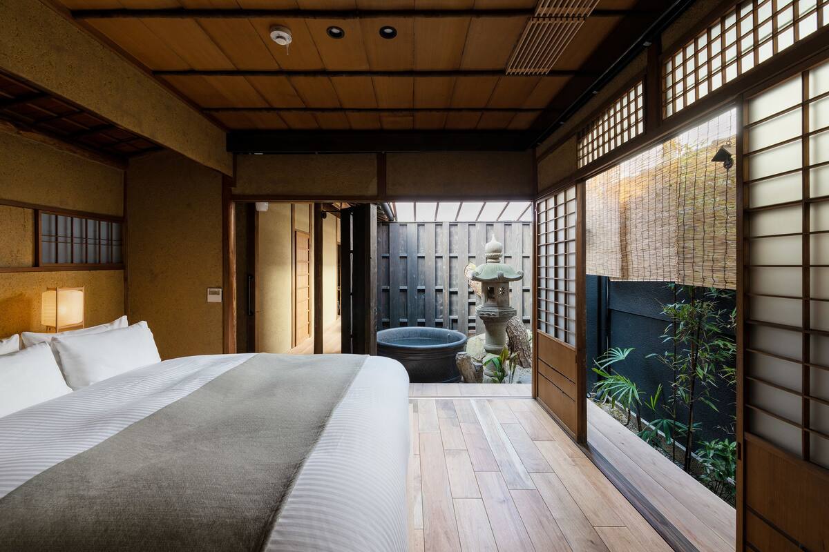 Une chambre de style japonais traditionnel, avec un sol recouvert de tatamis, un grand lit et une vue sur un jardin, visible à travers un paravent en papier de riz (shoji).