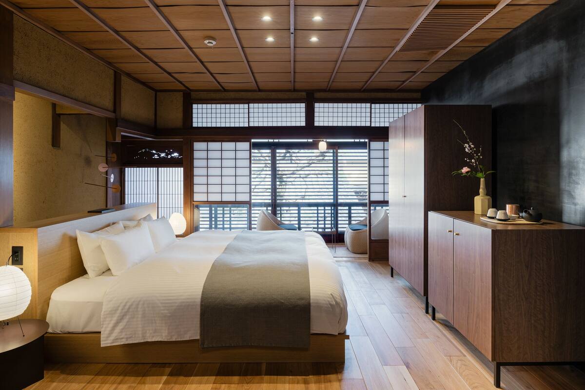 Une chambre moderne avec un grand lit, un plancher en bois et une vue sur la ville grâce à de grandes fenêtres.