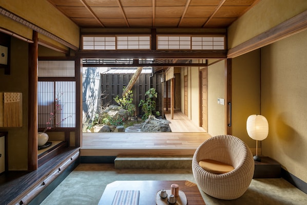 A traditional Japanese room with tatami flooring, a low wooden table, a woven chair, and a view of a garden through a shoji screen.