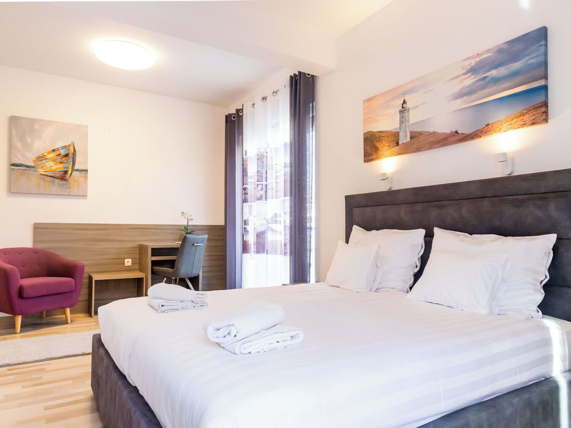A hotel room with a bed, a desk, a chair, and a painting on the wall.