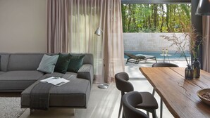 A modern living room with a grey sofa, a wooden dining table, and a view of an outdoor swimming pool. - Wonderful private villa for 20 guests with A/C, private pool, WIFI, TV and terrace (Umag)