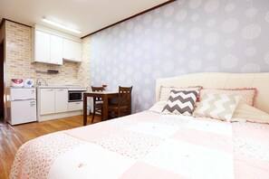 Une chambre à coucher avec un lit, des oreillers et une table de chevet. Il y a également un coin cuisine équipé d’un réfrigérateur, d’un four à micro-ondes et d’un évier.