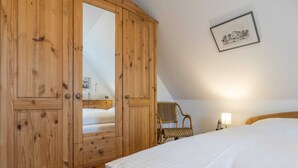 Ein Schlafzimmer mit einem Holzschrank, einem Bett, einem Stuhl und einem gerahmten Bild an der Wand.