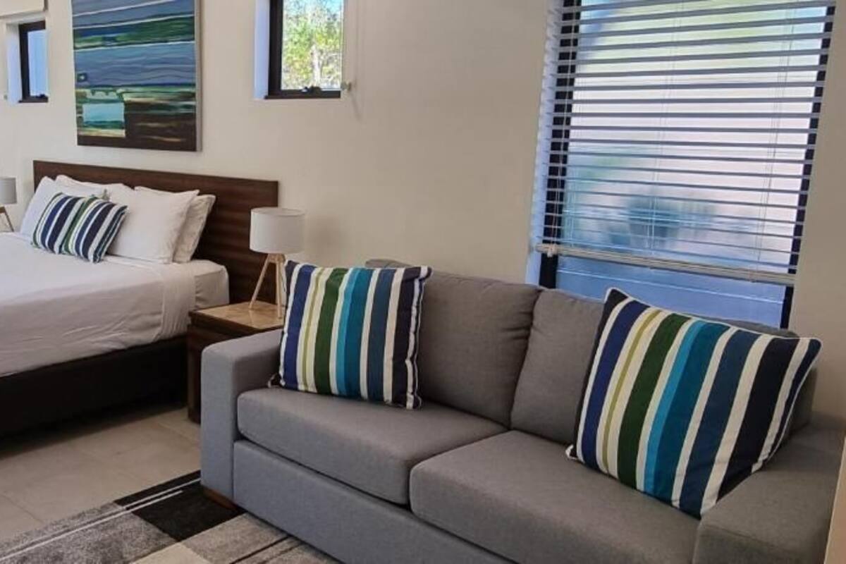 Quarto de hotel com cama, sofá, espelho redondo e quadro na parede.