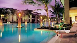 A swimming pool with lounge chairs and palm trees, surrounded by buildings with warm lighting.