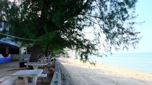 A beachside area with picnic tables and a building in the background. - Rungarun Resort (Chaiya)