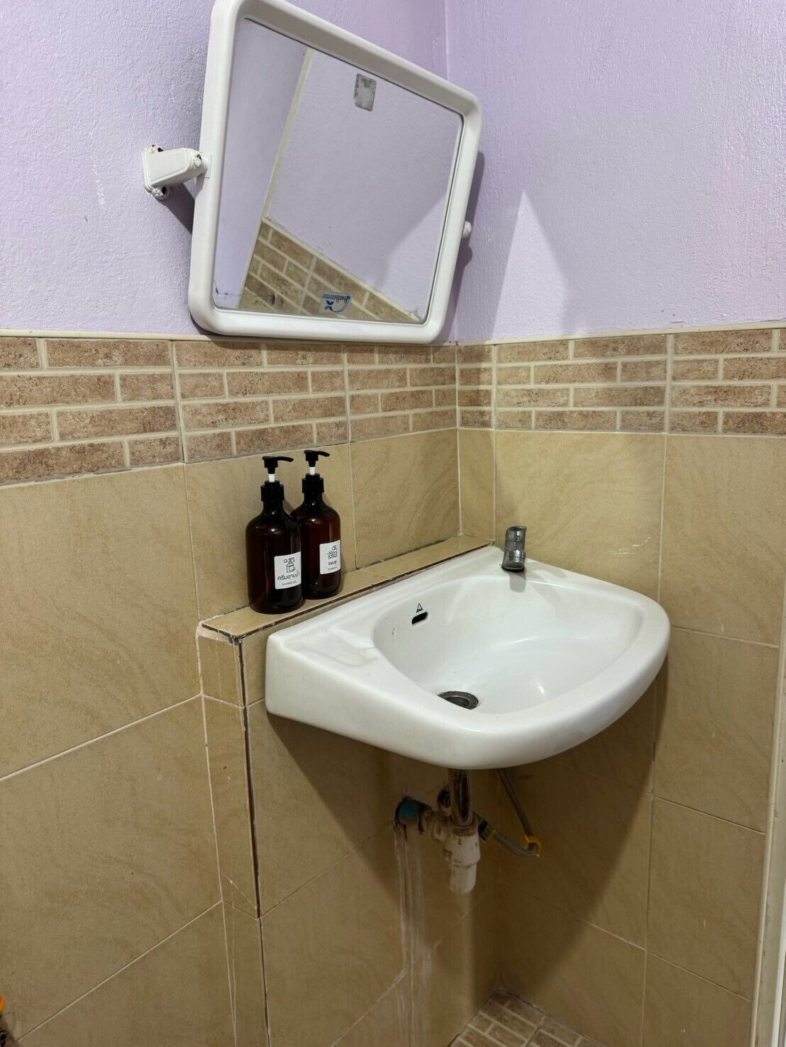 A bathroom with a white sink, two soap dispensers, a mirror, and a tiled wall.