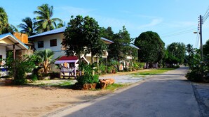 A residential street with houses, palm trees, and a clear sky. - Rungarun Resort (Chaiya)