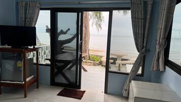 A room with a television on a stand, a sliding glass door leading to a beach, and a small table with chairs outside.